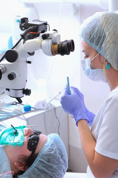 O dentista tem uma broca fina nas mãos. Uma broca para a passagem de canais dentários. Tratamento dentário com microscópio.Odontologia moderna. Foto vertical. — Fotografia de Stock