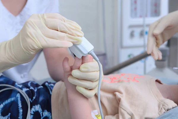 Lékař měří hladinu kyslíku v krvi pomocí přístroje. Pulzní oxymetr v rukou lékaře. Dítě je v anestézii.. — Stock fotografie