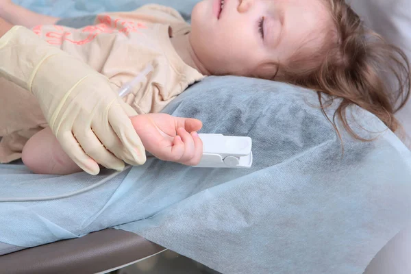 Egy gyerek pulzoximéterrel a karján. A gyerek a háttérben nincs fókuszban. Oxigénszint mérése a vérben. — Stock Fotó