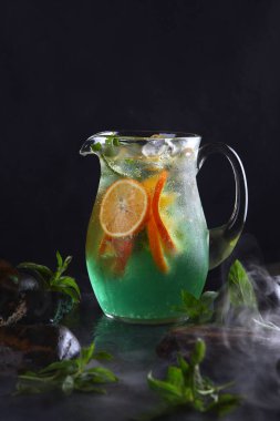 Klasik alkolsüz Mojito limonatası. Ev yapımı soğuk limonata. Cam sürahide taze meyve. Siyah arka plan. Dikey fotoğraf.