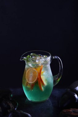 Klasik alkolsüz Mojito limonatası. Ev yapımı soğuk limonata. Cam sürahide taze meyve. Siyah arka plan. Dikey fotoğraf. Boşluğu kopyala.