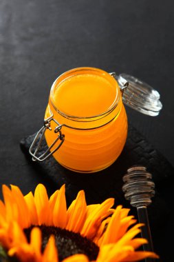 Siyah arka planda ballı cam kavanoz. Ayçiçeği. Dikey fotoğraf. Bal için cam çubuk. Yukarıdan bak. Uzayı kopyala Biyolojik ürün.