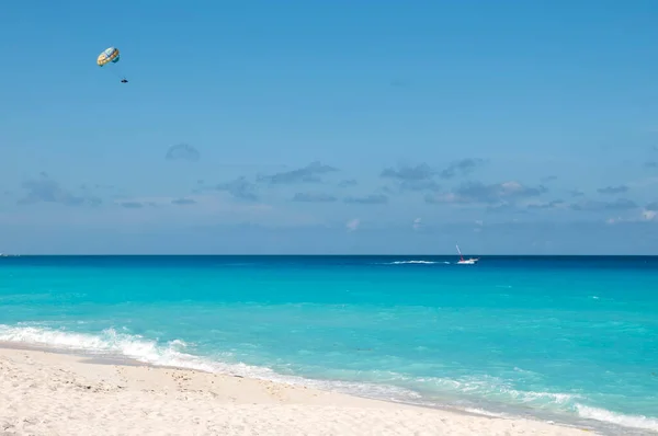 Meksika, Cancun 'da egzotik bir plajın yakınındaki tropikal denizde parasailing. Yaz eğlencesi ve eğlence aktiviteleri. Arka planda mavi gökyüzü ve çok az bulut