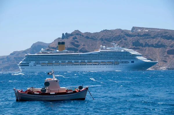 A cruise ship and a fishing boat sailing in the caldera of the island of Santorini in Greece. In the background the coast of Thirasia