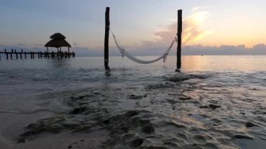 Gün batımında bir sahil turkuaz su üzerinde bir hamak ve Meksika 'daki Cozumel adasında beyaz kum.