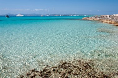 İspanya, Formentera 'daki Espalmador adasının panoramik manzarası. Arka planda lüks demirli tekneler ve mavi gökyüzü