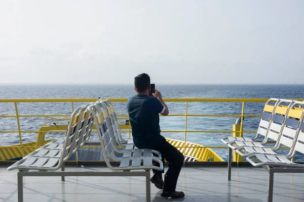 A man with his back turned, sitting in a ro-ro ferry talking on the phone looking at the horizon over the sea. Cozumel Island, Mexico