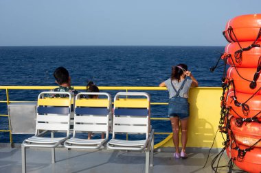 Denizde bir feribotta oturan üç yolcu Meksika kıyısı yakınlarındaki Karayip Denizi üzerindeki ufka bakıyor..