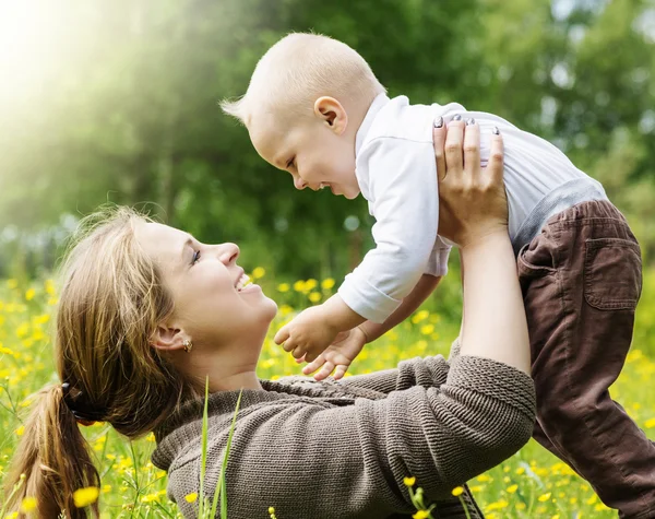 Familia feliz, madre levanta a su hijo en el fondo de la naturaleza — Foto de Stock