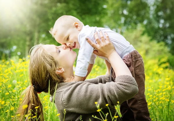 Mother lifts her son and kisses him on nature background — Stock Photo, Image