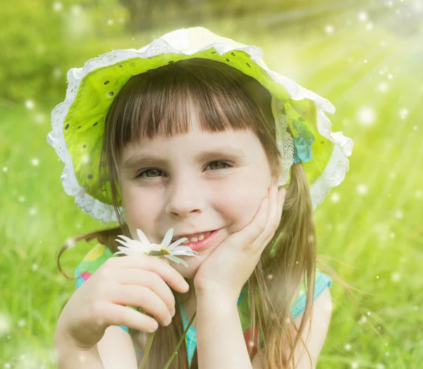 Красива маленька дівчинка на лузі, освітлена сонцем, тримає ромашку — стокове фото