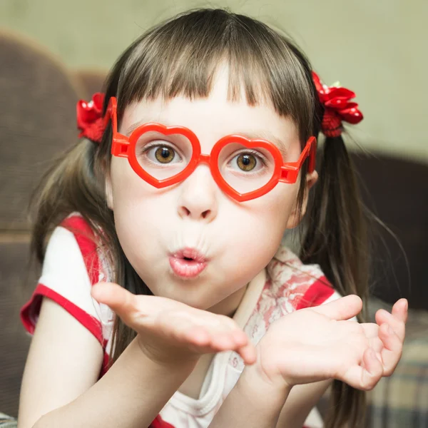 Милая маленькая девочка в очках в форме сердца посылает воздушный поцелуй — стоковое фото