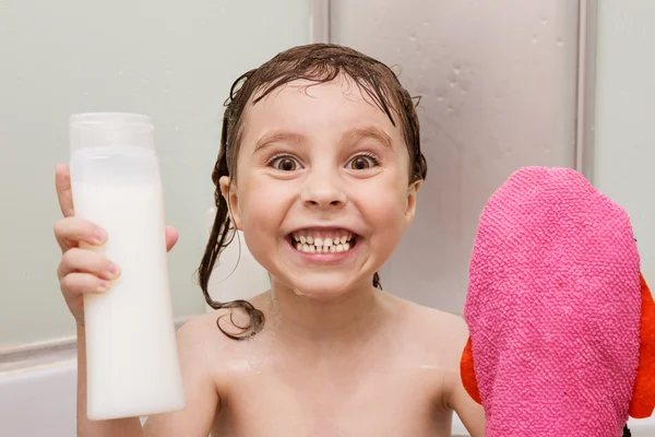 Menina sorridente no chuveiro com uma toalha e xampu em suas mãos — Fotografia de Stock