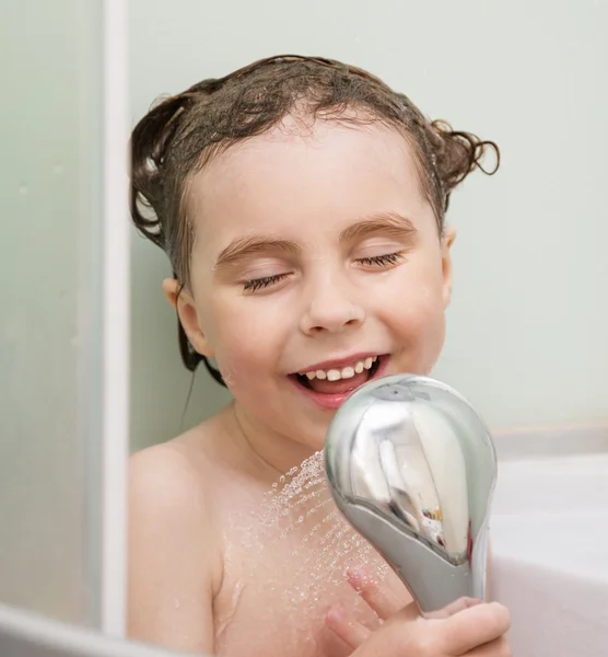 Vacker liten flicka häller vattnet från duschen i ett badrum stall — Stockfoto