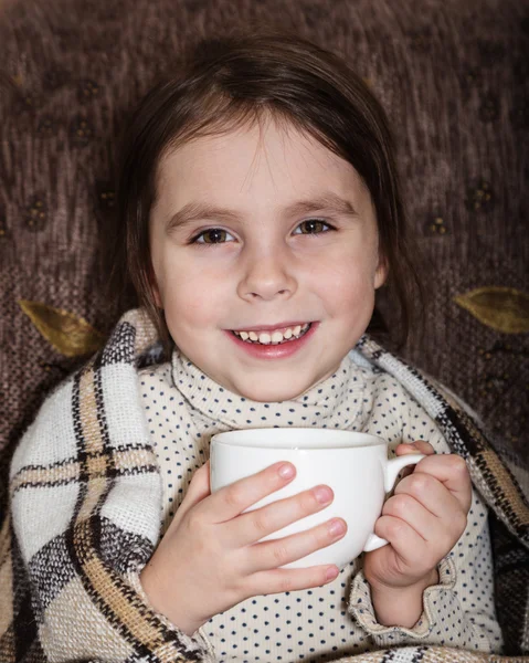 Niña sonriente envuelta en una manta bebiendo una taza de bebida caliente . —  Fotos de Stock