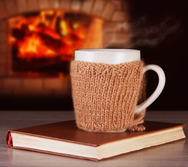 Varm dryck i en mugg som bär en Stickade kläder och gamla böcker på bakgrund av eldstaden. — Stockfoto