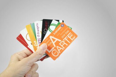 Female hand holding a bunch of French supermarket fidelity cards. Grey background. clipart