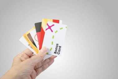 Female hand holding German store fidelity cards. Moemax, MediaMarkt and dm-drogerie markt between others. Grey background. clipart