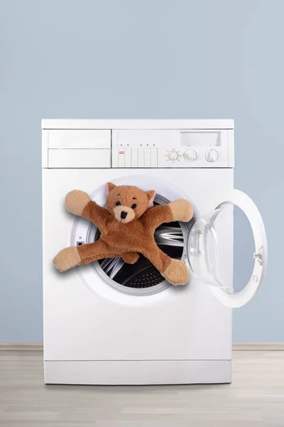 Soft toy refusing to get into the washing machine. Plain blue background. Hand-wash only or fear of bathing concept. Copy space.