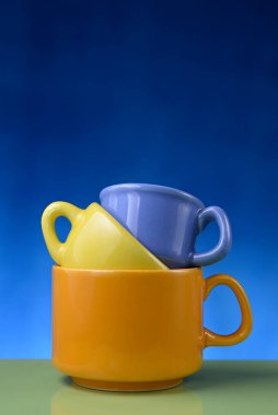 Cyan 'dan mavi gradyan arka plana üç farklı renk ve boyutta istiflenmiş bardak. Boşluğu kopyala.