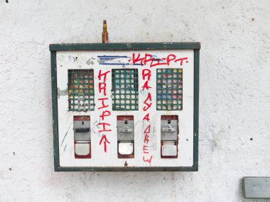 Duvarda eski bir sakız otomatı var. Makinede boş bir içki şişesi var. Açık hava, Almanya.