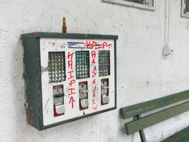 Üzerinde boş içki şişesi olan klasik bir sakız otomatı. Makinenin yanında ahşap bir bank. Her ikisi de grafiti ile kaplıydı. Sokakta açık bir duvar. Almanya.