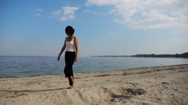 Güneşli bir günde sahilde kumsala giden mutlu yetişkin kadın. Arka planda sakin dalgalarla deniz kıyısında yürüyen güzel bir bayan. Yaz tatili ya da tatil kavramı. Yavaş çekim