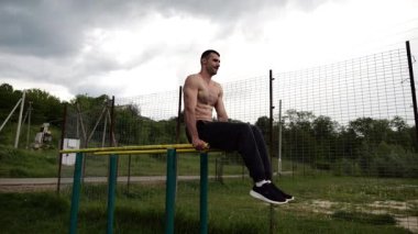 Spor alanında paralel barlarda karın kaslarını çalıştıran güçlü bir adam. Genç üstsüz sporcu doğada egzersiz yapıyor. Doğada spor yapan sporcu. Aktif spor yaşam tarzı kavramı.