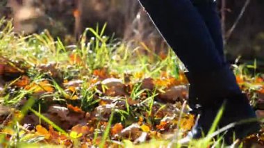 Düşük görüşlü, kadın ayaklı, kurumuş yaprakların üzerinde iz süren. Genç bayanın bacakları dışarı doğru adım atıyor. Güneşli bir sonbahar gününde doğada yürüyen bir kız. Yavaş çekim