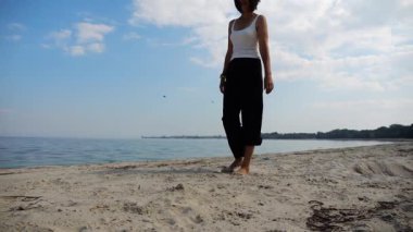 Güneşli bir günde sahilde kumsala giden mutlu yetişkin kadın. Arka planda sakin dalgalarla deniz kıyısında yürüyen güzel bir bayan. Yaz tatili ya da tatil kavramı. Yavaş çekim