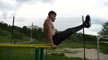 Güçlü bir adam karın kaslarını eğitir spor sahasında paralel barlarda bacak kaldırır. Genç üstsüz sporcu doğada egzersiz yapıyor. Doğada spor yapan sporcu. Sportif yaşam tarzı kavramı.