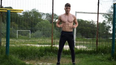 Spor sahasında çömelme hareketleri yapan erkek üstsüz atlet. Yaz doğasında çalışan genç bir sporcu. Güçlü sporcu dışarıda egzersiz yapıyor. Aktif ve sportif yaşam tarzı kavramı. Yavaş çekim
