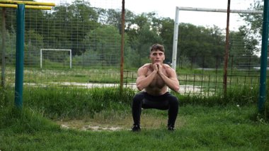 Spor sahasında çömelme hareketleri yapan erkek üstsüz atlet. Yaz doğasında çalışan genç bir sporcu. Güçlü sporcu dışarıda egzersiz yapıyor. Aktif ve sportif yaşam tarzı kavramı. Yavaş çekim