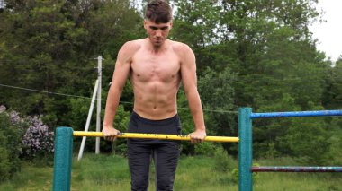 Cesur üstsüz sporcu doğada yatay çıtada şınav çekiyor. Güçlü ve kaslı adam spor alanında antrenman yapıyor. Genç atletik adam dışarıda egzersiz yapıyor. Aktif ve sağlıklı yaşam tarzı kavramı.