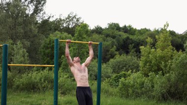 Spor sahasında barfiks çeken kaslı bir sporcu. Genç üstsüz sporcu doğada egzersiz yapıyor. Güçlü sporcu adam dışarıda antrenman yapıyor. Sağlıklı ve aktif yaşam tarzı kavramı. Yavaş çekim