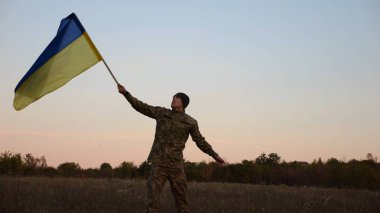 Erkek asker, Rusya 'nın işgal ettiği özgür bölgede mavi-sarı bayrak sallıyor. Ukrayna ordusunun genç askeri, hava kararırken Rus saldırısına karşı kazanılan zaferin şerefine Ukrayna bayrağı kaldırdı..