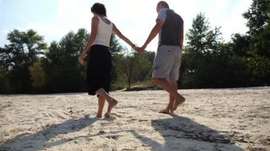 Romantik çift el ele tutuşup kumsalda yürüyor. Güneşli bir günde kıyıya giden mutlu bir çift. Sevgililer tatil köyünde birlikte vakit geçirirler. Yaz tatili veya tatil kavramı.