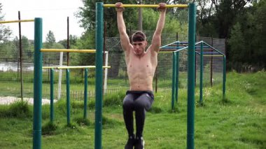 Spor sahasında karın kaslarını çalıştıran güçlü bir adam. Genç sporcu, barfiks çekme çubuğunda egzersiz yapıyor. Doğada spor yapan sporcu. Sportif yaşam tarzı kavramı.