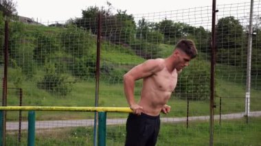 Genç sporcu doğada paralel barlarda şınav çekiyor. Spor alanında egzersiz yapan güçlü bir sporcu. Erkek üstsüz sporcu dışarıda sıkı çalışıyor. Aktif spor yaşam tarzı kavramı. Yavaş çekim