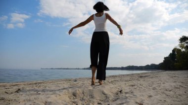 Güneşli bir günde sahil kenarında kumsalda yürüyen güzel bir bayan. Mutlu yetişkin kadın kıyı şeridine doğru dönüyor. Kaygısız kadın deniz kenarında dinleniyor. Yaz tatili veya tatil kavramı