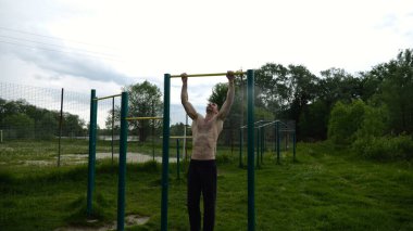 Spor sahasında barfiks çeken kaslı bir sporcu. Genç üstsüz sporcu doğada egzersiz yapıyor. Güçlü sporcu adam dışarıda antrenman yapıyor. Sağlıklı ve aktif yaşam tarzı kavramı. Yavaş çekim