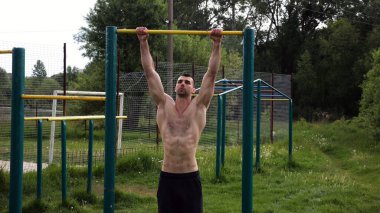 Spor sahasında barfiks çeken kaslı bir sporcu. Genç üstsüz sporcu doğada egzersiz yapıyor. Güçlü sporcu adam dışarıda antrenman yapıyor. Sağlıklı ve aktif yaşam tarzı kavramı. Yavaş çekim