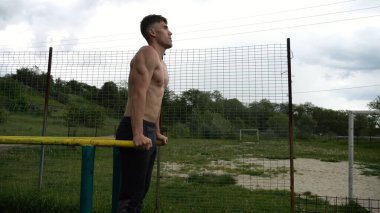 Genç sporcu doğada paralel barlarda şınav çekiyor. Spor alanında egzersiz yapan güçlü bir sporcu. Erkek üstsüz sporcu dışarıda sıkı çalışıyor. Aktif spor yaşam tarzı kavramı. Yavaş çekim