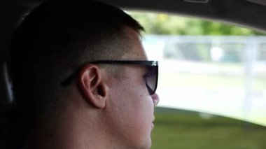 Profile of confident man driving a motor car at town. Male face of male driver in sunglasses looking concentrated to urban road while riding automobile. Slow mo