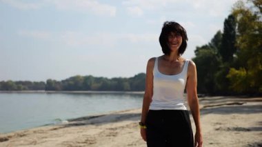 Güneşli bir günde sahil kenarında kumsalda yürüyen güzel bir bayan. Mutlu yetişkin kadın kıyı şeridine doğru dönüyor. Kaygısız kadın deniz kenarında dinleniyor. Yaz tatili veya tatil kavramı.