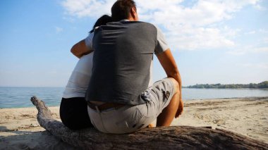 Kumsalda tahta kütüğün üzerinde otururken mutlu çift kucaklaşması. Güneşli bir günde deniz manzarasına hayran olan romantik bir çift. Sevgililer tatil köyünde birlikte vakit geçirirler. Yaz tatili ya da tatil kavramı. Yavaş çekim