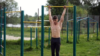 Spor sahasında barfiks çeken kaslı bir sporcu. Genç üstsüz sporcu doğada egzersiz yapıyor. Güçlü sporcu adam dışarıda antrenman yapıyor. Sağlıklı ve aktif yaşam tarzı kavramı. Yavaş çekim