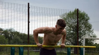 Erkek üstsüz sporcu doğada paralel barlarda şınav çekiyor. Spor alanında egzersiz yapan güçlü bir sporcu. Genç sporcu dışarıda sıkı çalışıyor. Aktif spor yaşam tarzı kavramı. Yavaş çekim