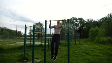 Spor sahasında barfiks çeken kaslı bir sporcu. Genç üstsüz sporcu doğada egzersiz yapıyor. Güçlü sporcu adam dışarıda antrenman yapıyor. Sağlıklı ve aktif yaşam tarzı kavramı. Yavaş çekim