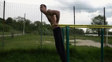 Genç sporcu doğada paralel barlarda şınav çekiyor. Spor alanında egzersiz yapan güçlü bir sporcu. Erkek üstsüz sporcu dışarıda sıkı çalışıyor. Aktif spor yaşam tarzı kavramı. Yavaş çekim